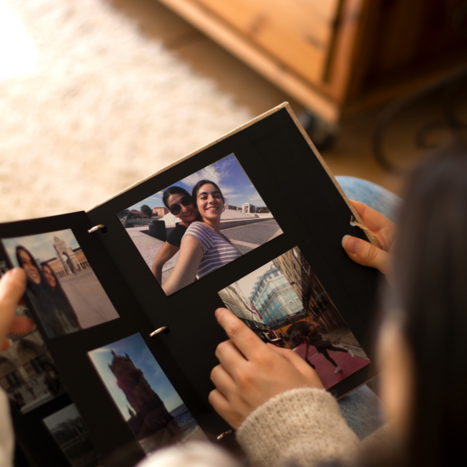 Hands hold a photo album with travel photos. Cozy indoor setting with a warm wooden background. Focus on images, bright and vivid.