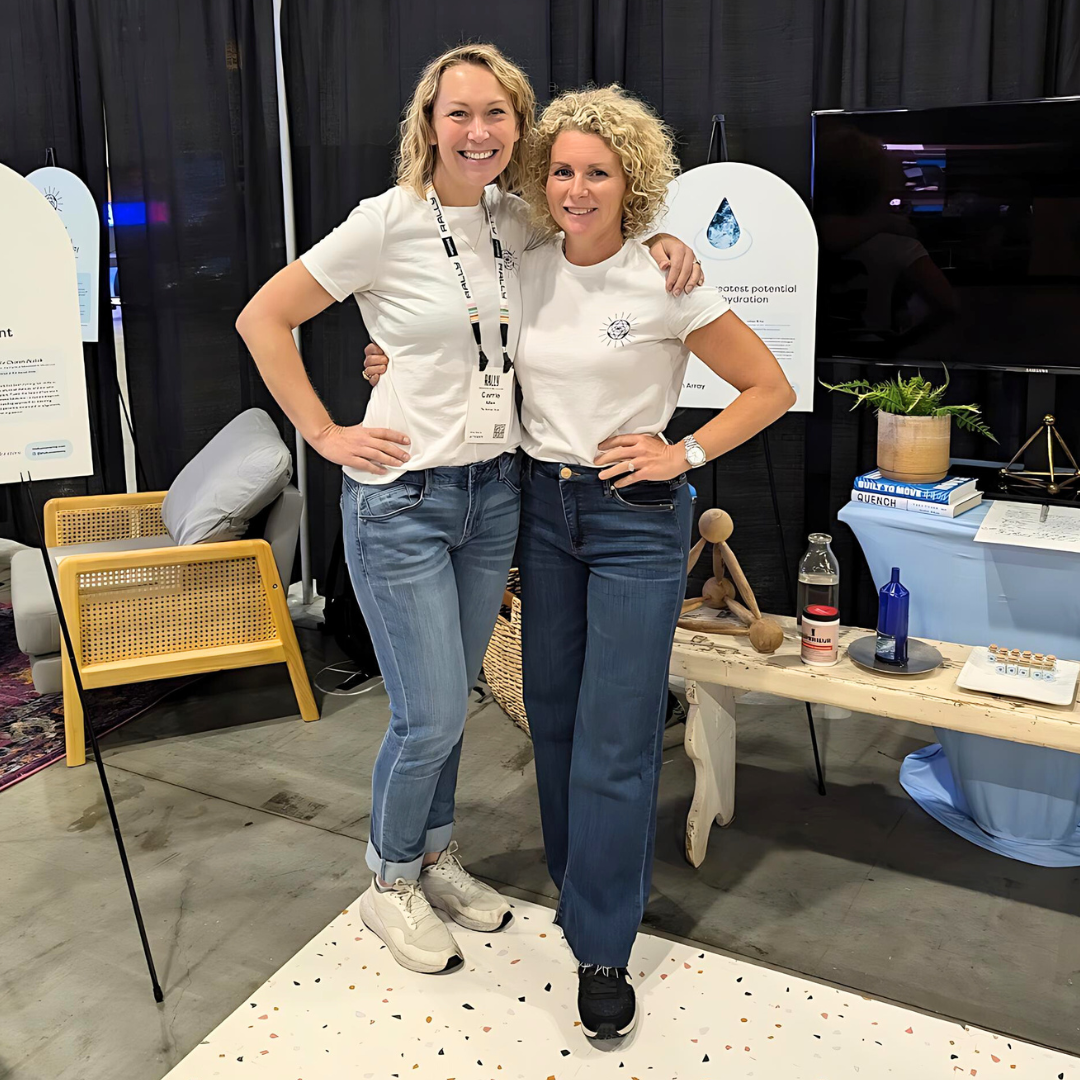 Two people standing in front of a conference center booth with their arms around each other.